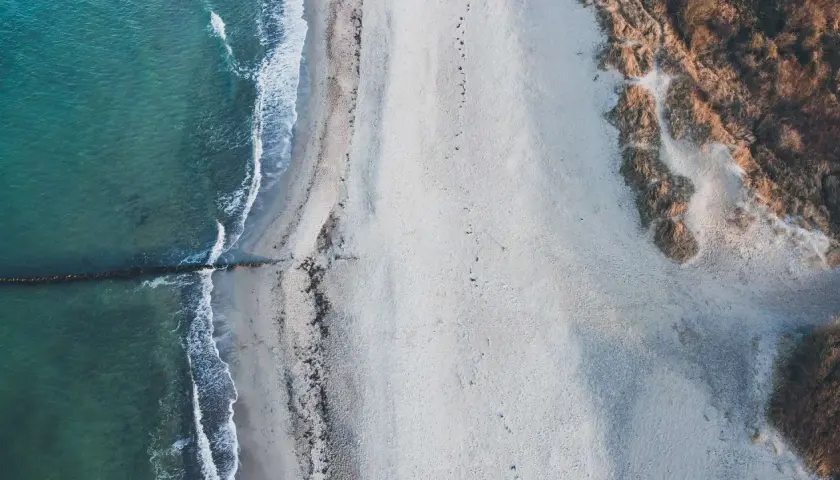 Puste plaże nad morzem, gdzie fale delikatnie muskają piasek, a wydmy porośnięte trawą tworzą naturalną granicę.