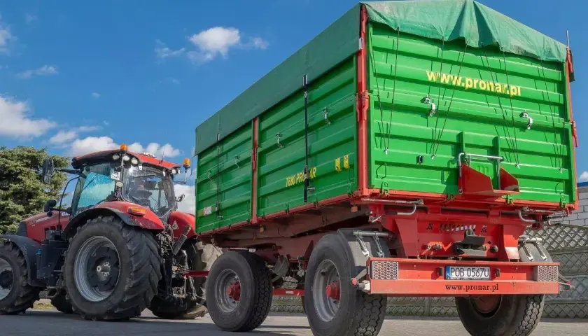 Czerwony traktor z zieloną przyczepą. Dowiedz się, jakich przyczep nie trzeba rejestrować, by sprawnie pracować w polu.