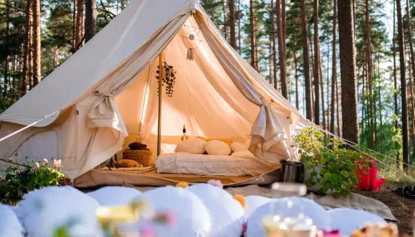 Wygodny namiot w lesie, z łóżkiem i dekoracjami, to właśnie glamping co to jest – luksusowy kemping.