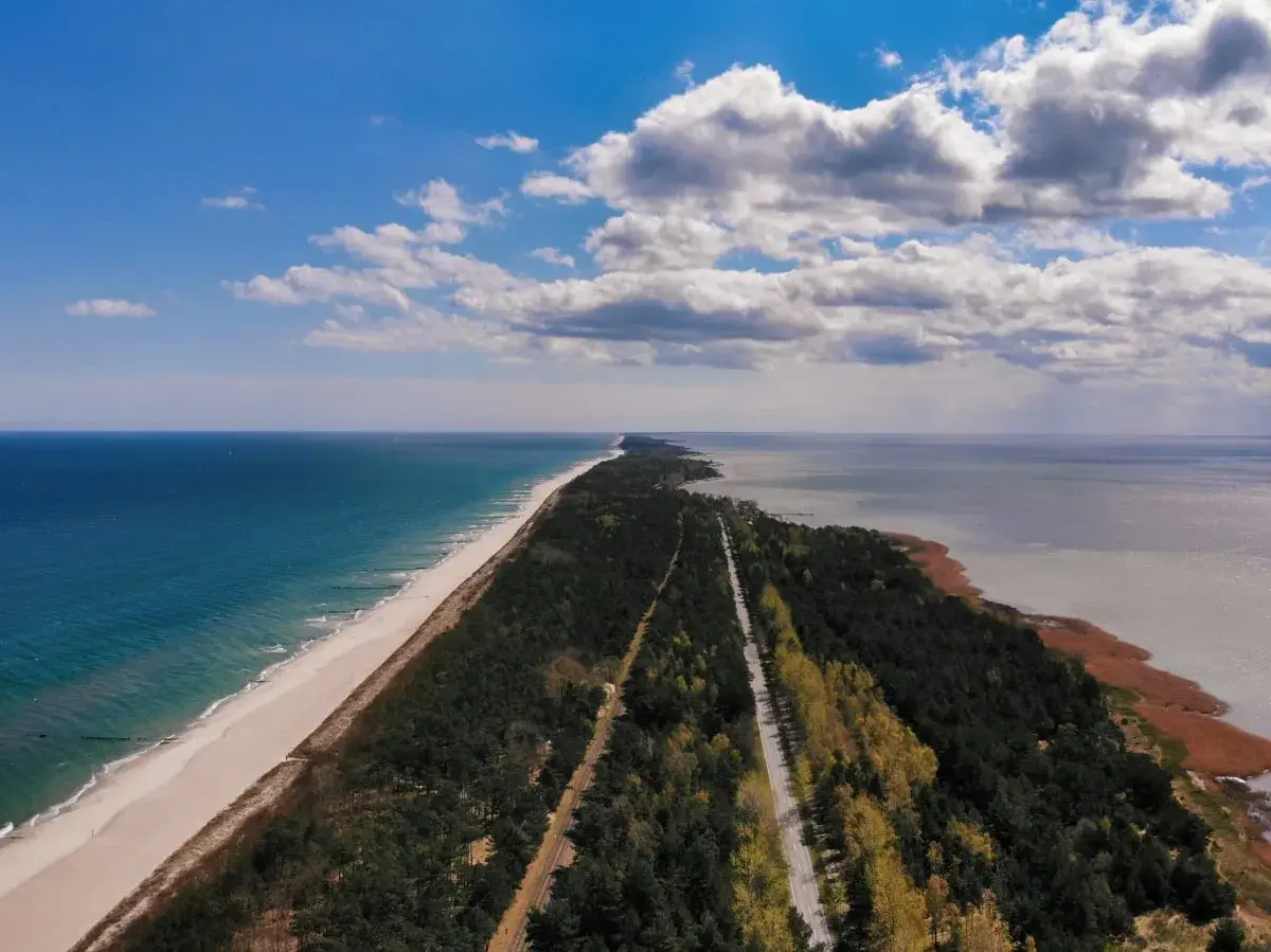 Długa, piaszczysta plaża i las otaczają drogę prowadzącą do morza. Idealne miejsce na parking z widokiem na morze.