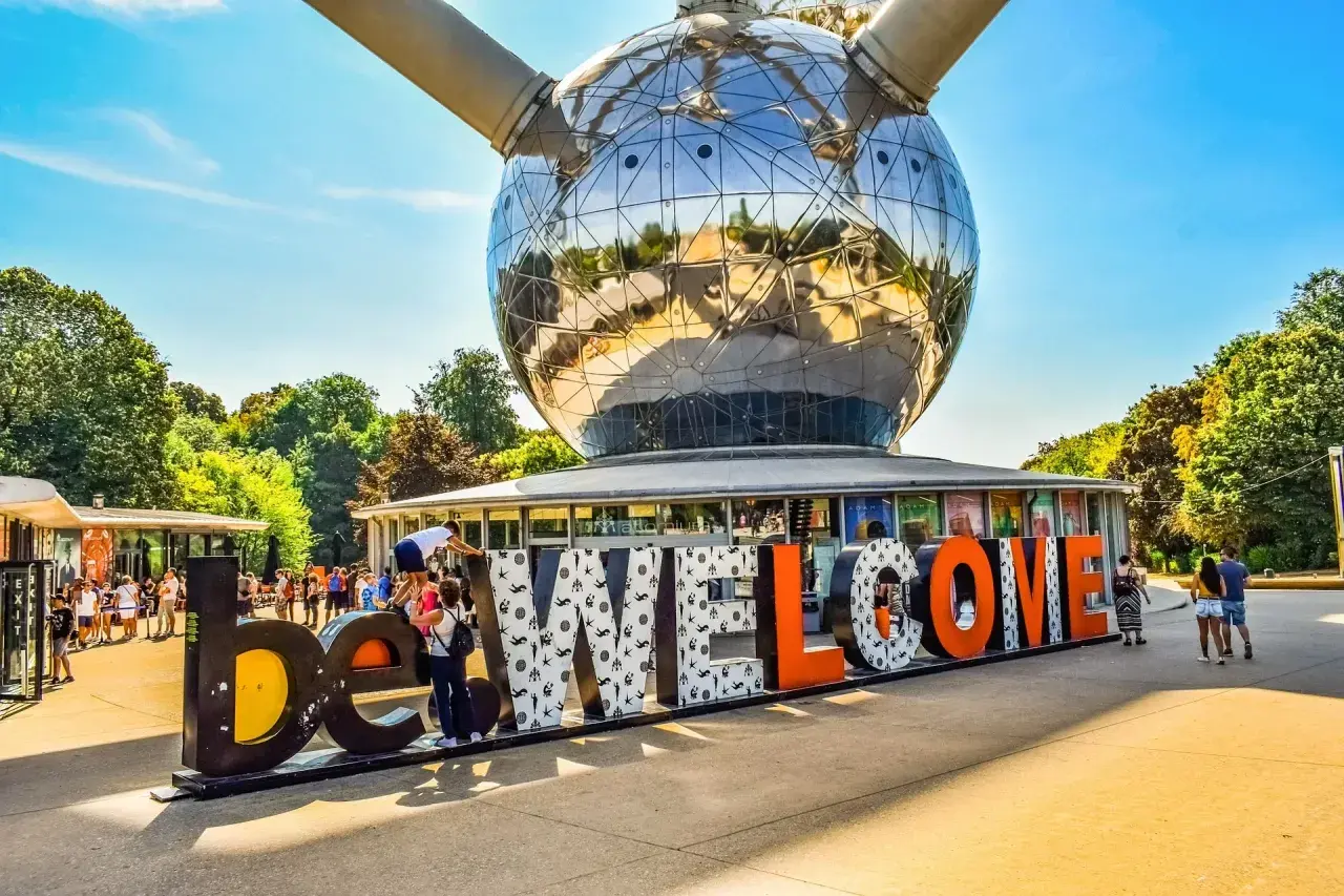 Bruksela nietypowe miejsca: Atomium wita turystów napisem "WELCOME". Słońce odbija się w stalowej kuli, a ludzie spacerują wokół.