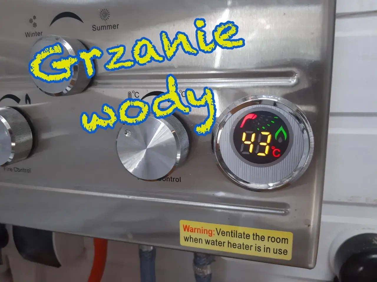 Grzanie wody w przyczepie kempingowej. Cyfrowy wyświetlacz pokazuje 43°C. Pokrętła do regulacji temperatury i kontroli ognia.