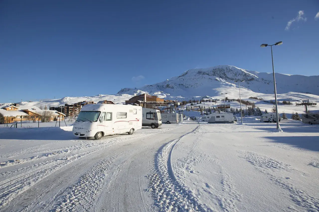 Zimowy parking w Alpe d'Huez, pełen kamperów, pod ośnieżonymi szczytami.