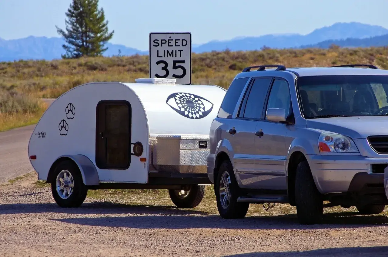 Srebrny SUV z przyczepą kempingową "Little Guy" pod znakiem ograniczenia prędkości do 35. Czy mając C+E można jeździć B+E? Tak, uprawnienia C+E obejmują B+E.