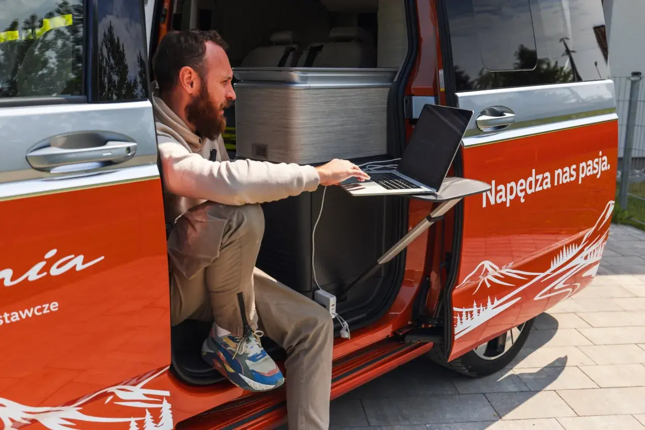 Mężczyzna pracuje na laptopie przy otwartych drzwiach kampera. Idealne miejsce na podróż kamperem, by połączyć pracę z przygodą.