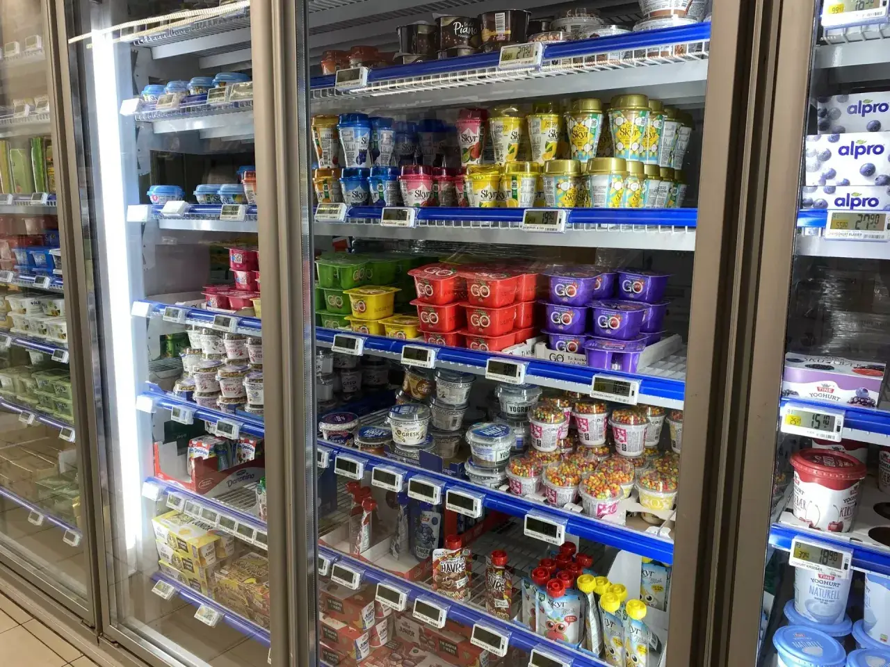 Lodówka pełna jogurtów i deserów. Widać różne marki i smaki, a także ceny, co daje pogląd na ceny w Norwegii jedzenie.