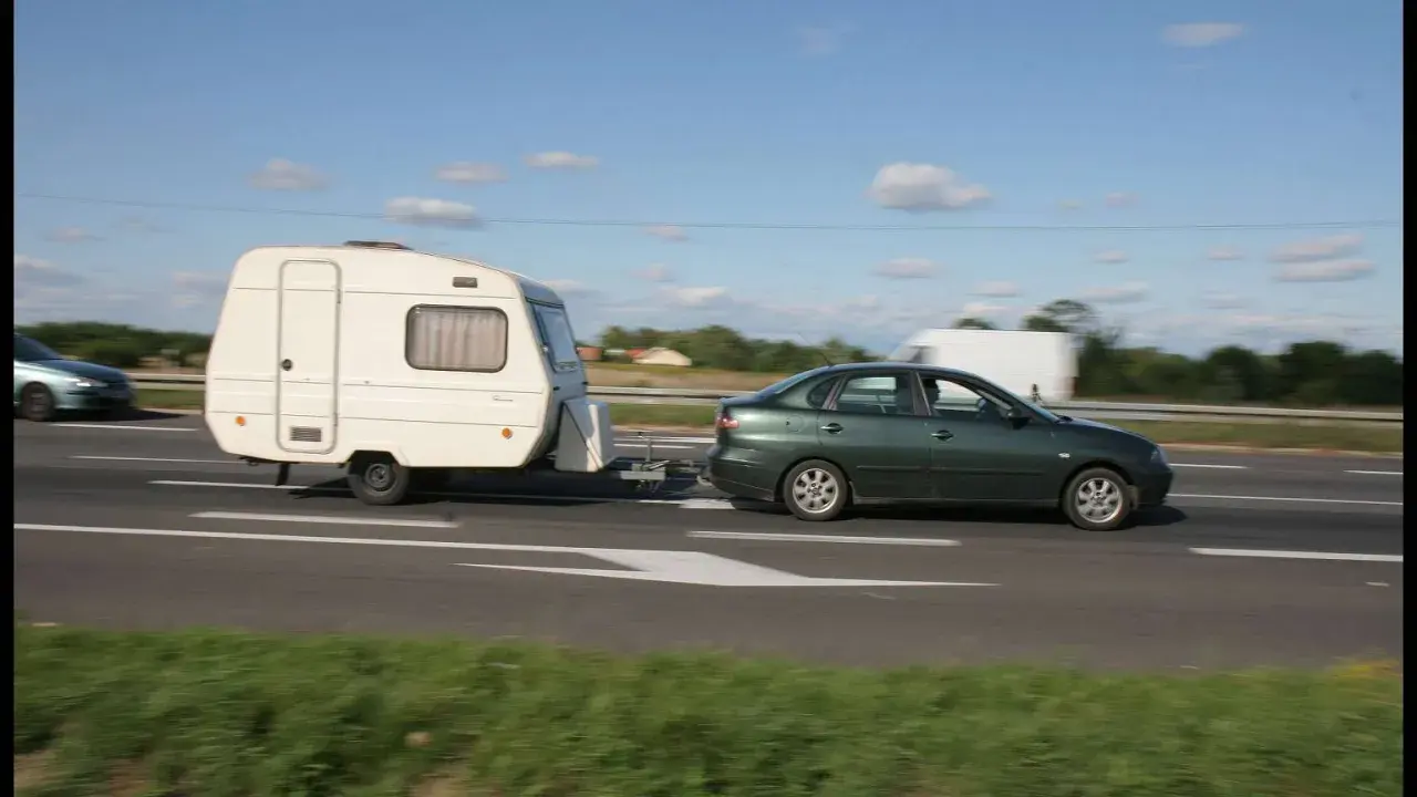 Zielony samochód ciągnie przyczepę kempingową. Ważne jest, jak obliczyć DMC zespołu pojazdów, by podróżować bezpiecznie.