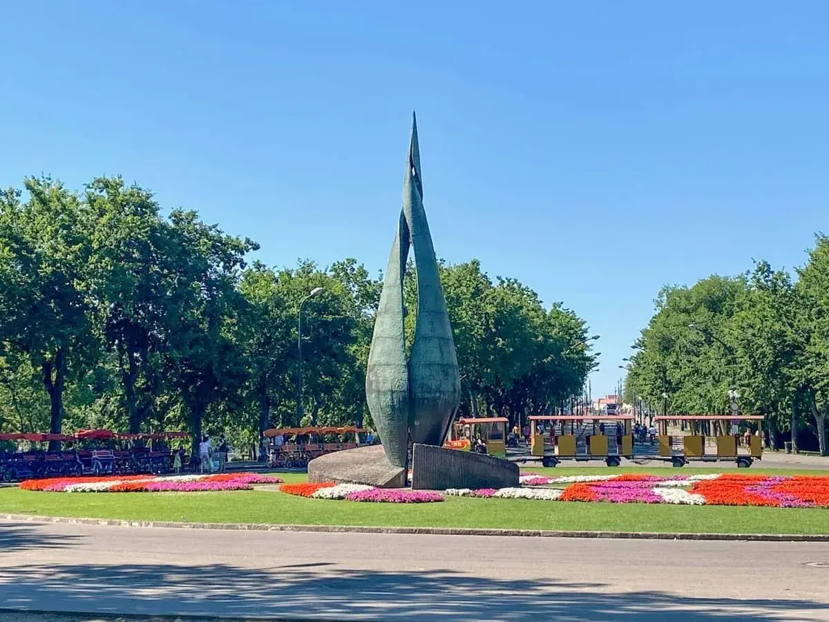 Rzeźba na Margit Sziget w Budapeszcie z kolorowymi kwiatami i turystycznymi pojazdami.