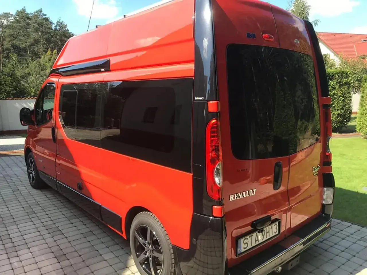 Pomarańczowy Renault Trafic L2H2 z przyciemnianymi szybami stoi na podjeździe z kostki brukowej.