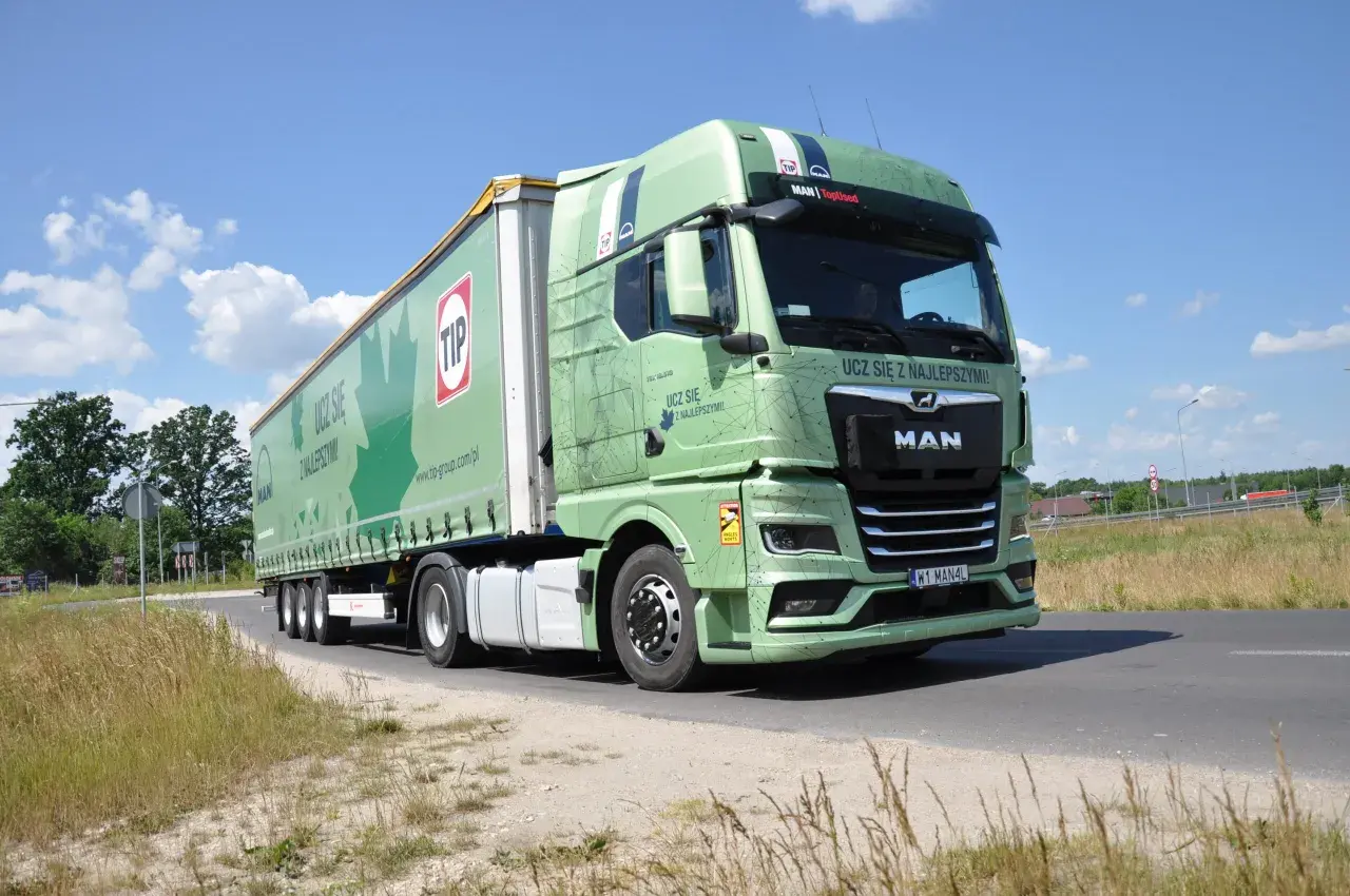 Zielona ciężarówka MAN z naczepą TIP na drodze. Długość zestawu c+e robi wrażenie, idealna do transportu.