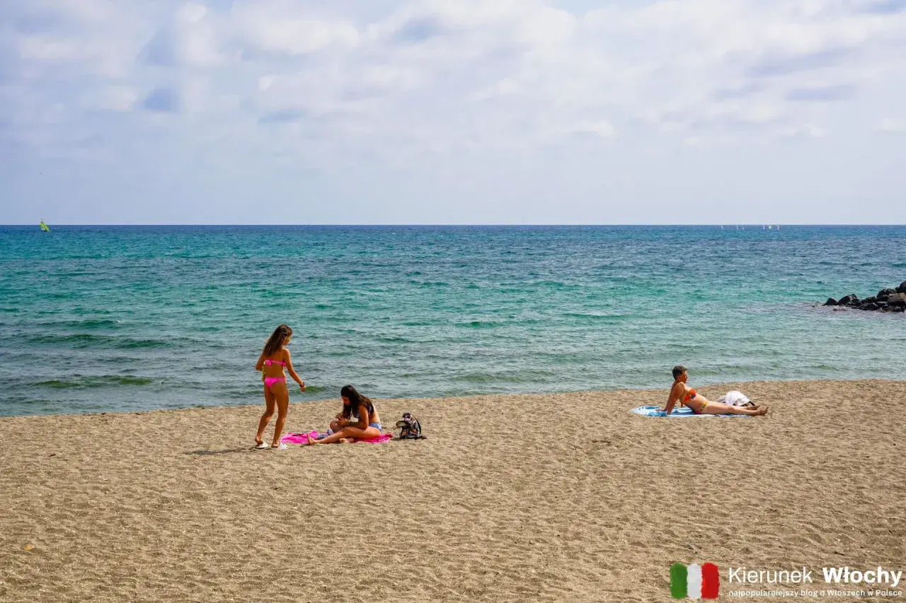 Trzy kobiety relaksują się na piaszczystych plażach Ostii. W tle błękitne morze i kilka żaglówek.