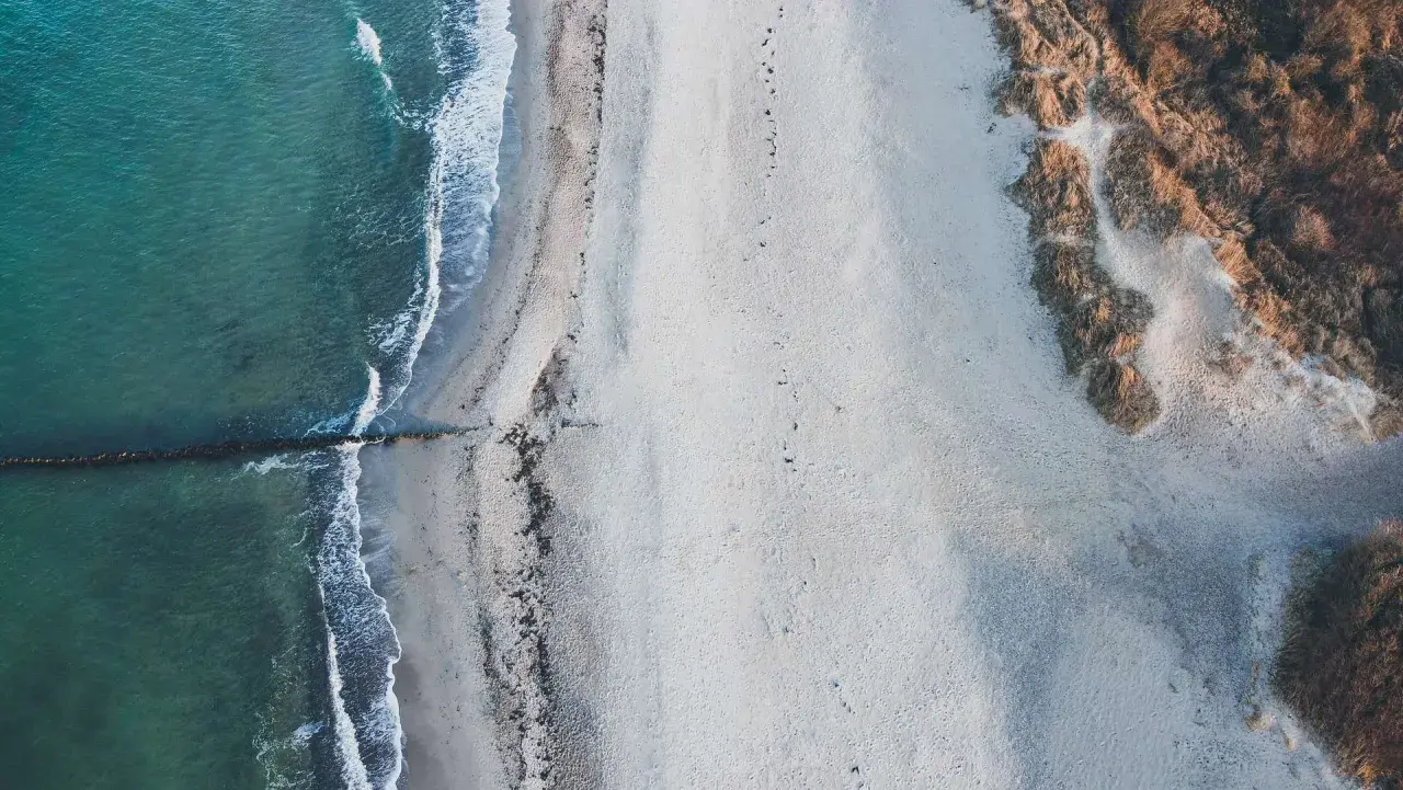 Puste plaże nad morzem, gdzie fale delikatnie muskają piasek, a wydmy porośnięte trawą tworzą naturalną granicę.