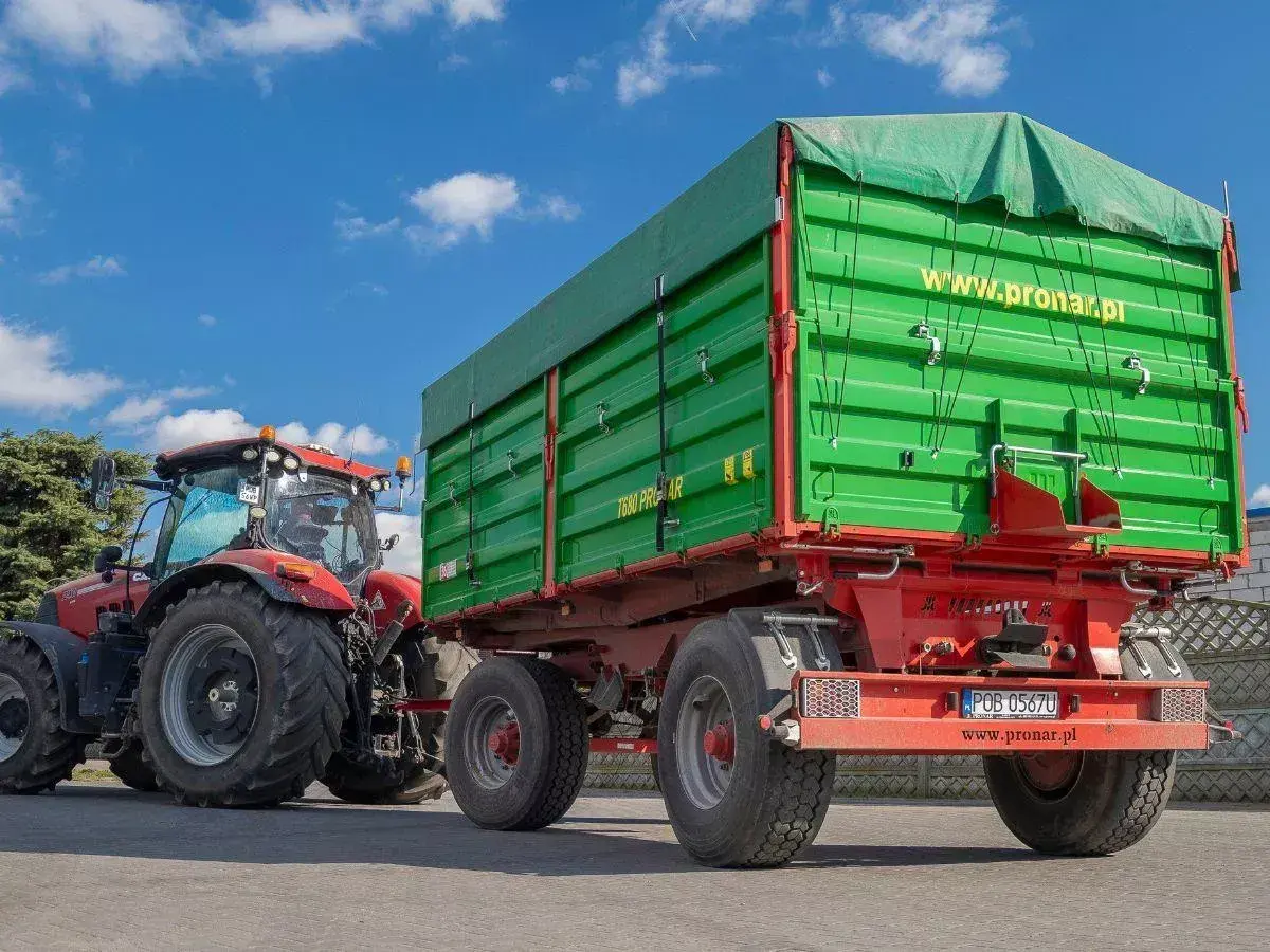 Czerwony traktor z zieloną przyczepą. Dowiedz się, jakich przyczep nie trzeba rejestrować, by sprawnie pracować w polu.
