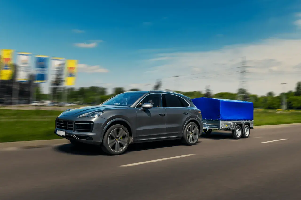 Szary SUV z przyczepą pod niebieską plandeką toczy się po autostradzie.