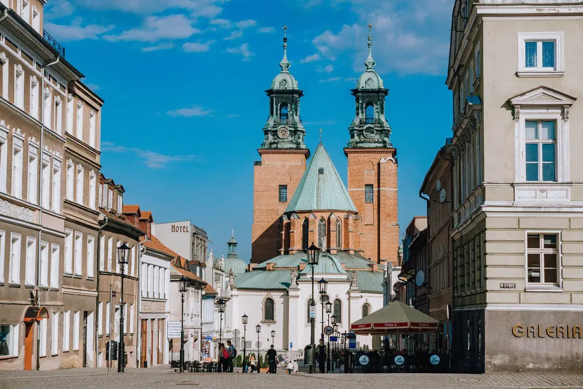 Rynek w Gnieźnie z katedrą w tle. Jasny, słoneczny dzień, błękitne niebo z chmurkami.