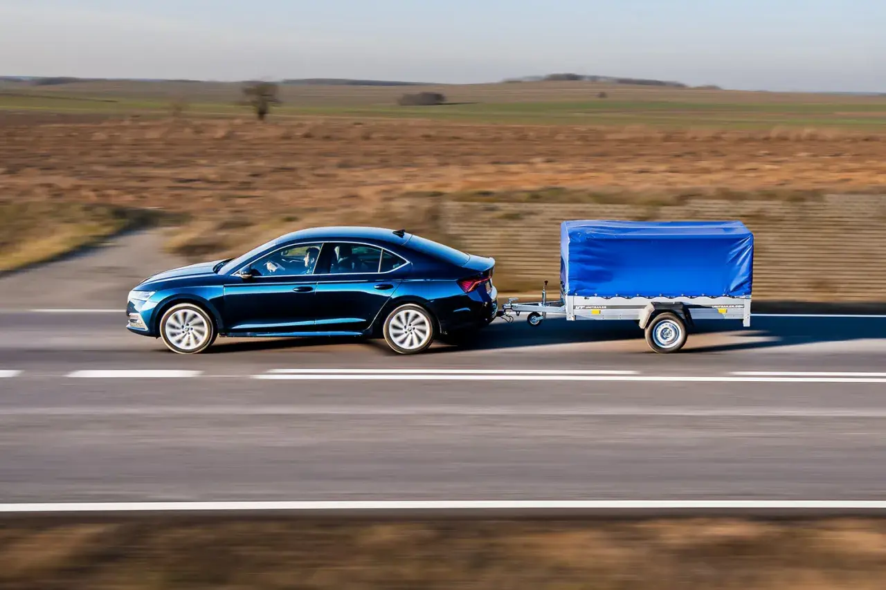 Ciemnoniebieski sedan ciągnie przyczepę z niebieską plandeką. Może to być sytuacja, gdy dmc przyczepy większe niż w dowodzie, ale wygląda na stabilną.