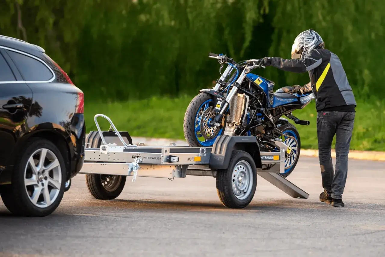 Mężczyzna w kasku ładuje motocykl na przyczepę. Dowiedz się, jakich przyczep nie trzeba rejestrować, by przewieźć sw&oacute;j sprzęt.