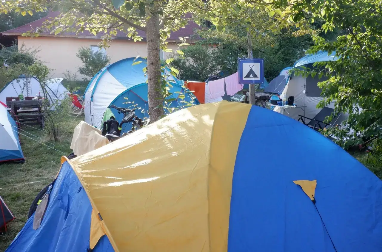 Kolorowy namiot bez zgłoszenia na kempingu, obok innych namiot&oacute;w i roweru.