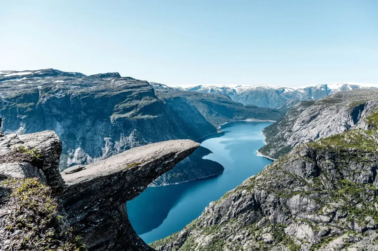 Niesamowita Norwegia, skała Trolla wystaje nad błękitną wodą fiordu. Majestatyczne g&oacute;ry otaczają ten cud natury.