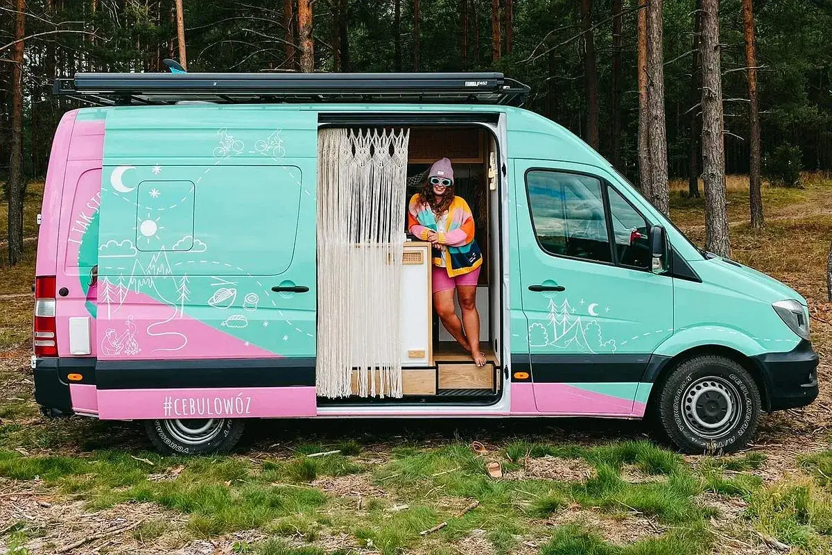 Przeróbka busa na kampera przepisy – kolorowy van z rysunkami, w którym stoi uśmiechnięta kobieta. #Cebulowóz gotowy na przygody!