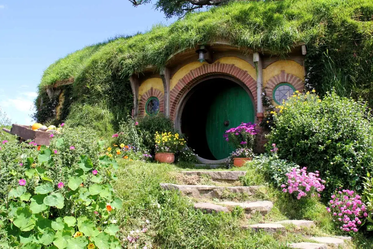 Urocza wioska hobbit&oacute;w z zielonymi drzwiami i kwitnącymi kwiatami.