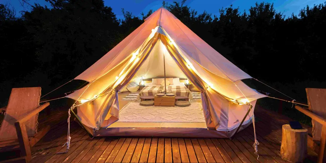 Nocne niebo, oświetlony namiot z wygodnym ł&oacute;żkiem i dywanem. To właśnie glamping co to jest &ndash; luksusowy kemping w otoczeniu natury.