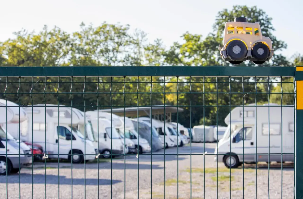 Zabawkowy kamper na płocie strzeże bezpiecznego parkingu kamper&oacute;w.