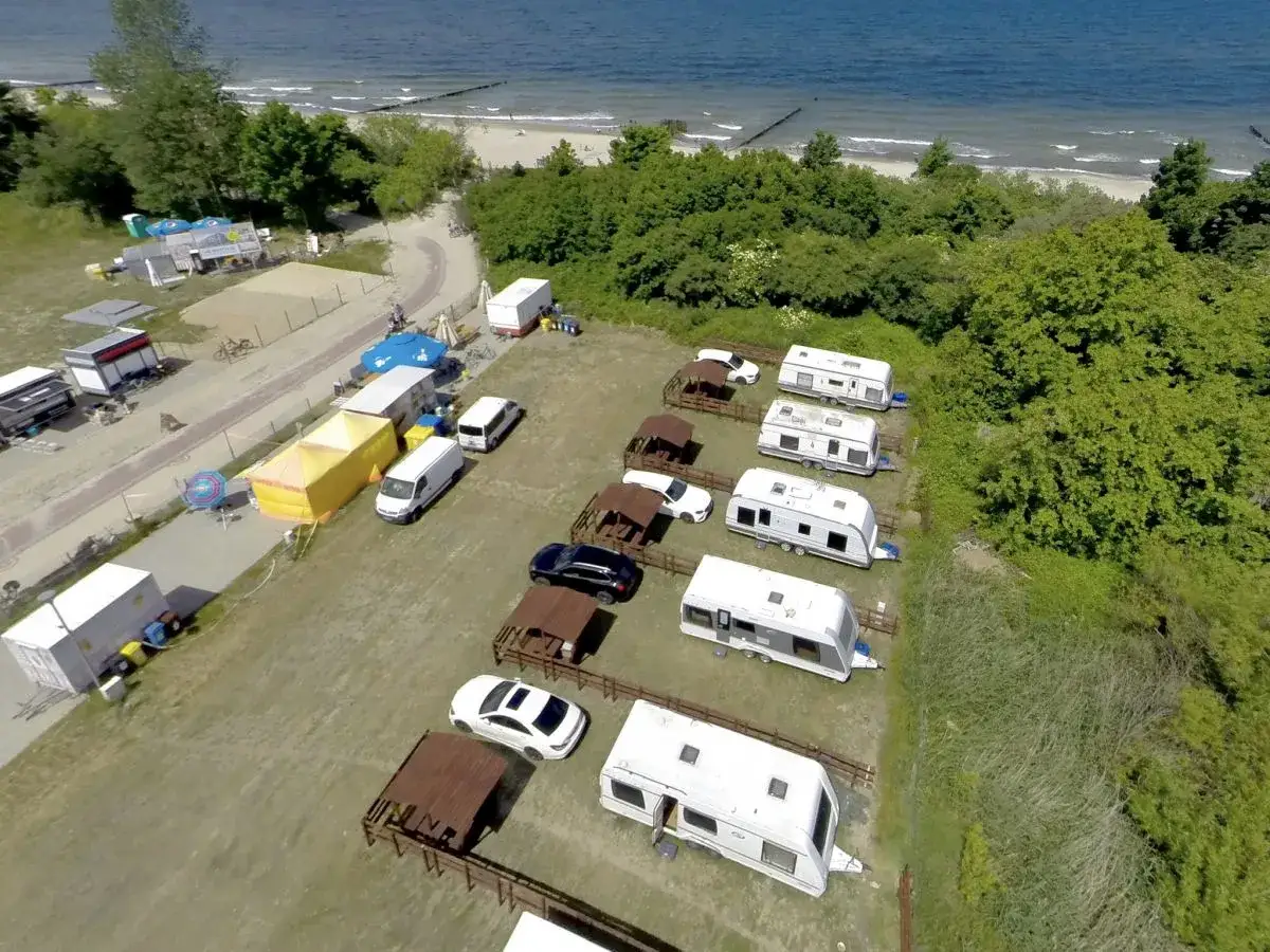 Przyczepy kempingowe nad morzem, gotowe na wakacyjny wypoczynek. W tle widać plażę i błękitne morze.