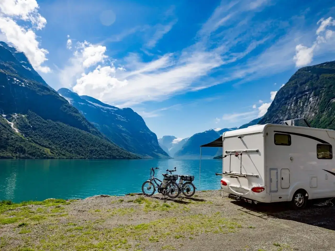 Kamper i Norwegii latem, nad turkusowym jeziorem, z rowerami gotowymi do zwiedzania górskich krajobrazów.