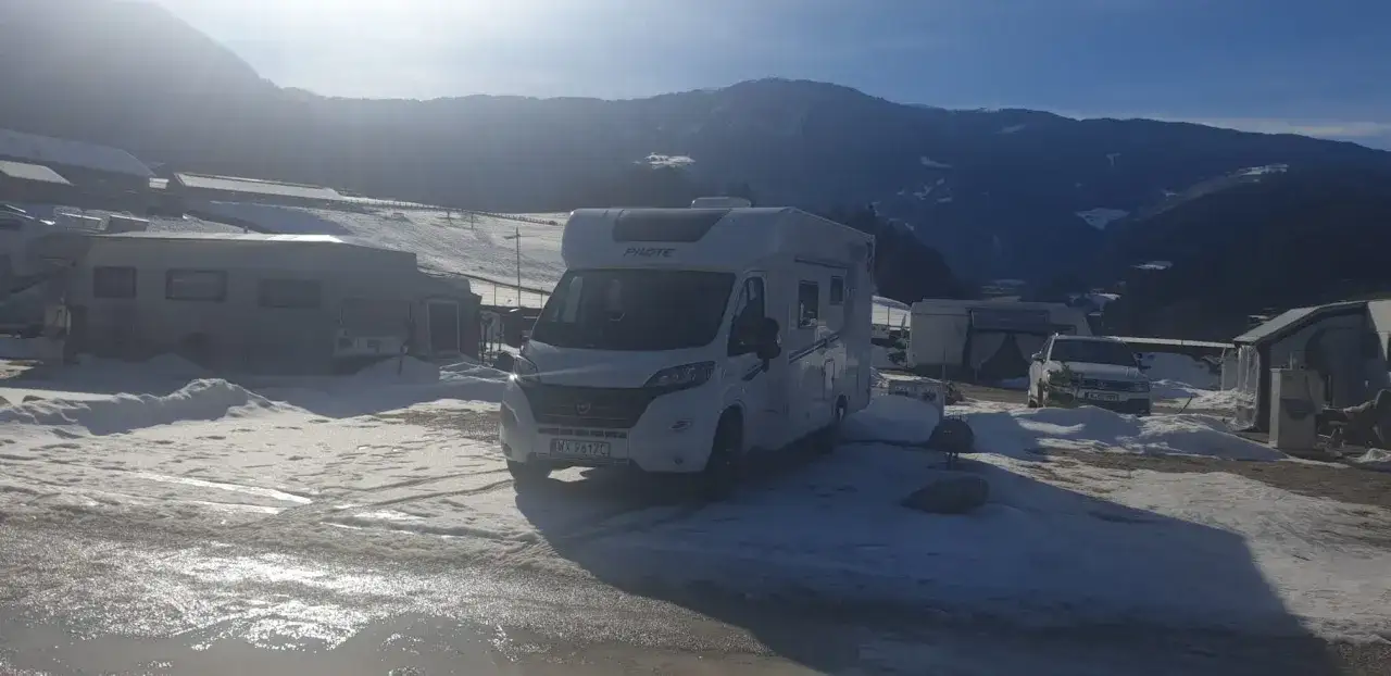Kamper i inne pojazdy kempingowe na śnieżnym polu namiotowym. G&oacute;ry w tle. Piękna łeba zimą.