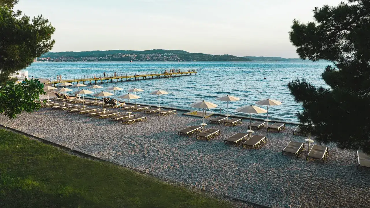 Słoneczne Słowenia plaże z leżakami i parasolami, w tle molo i wybrzeże.