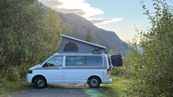 Kamper z podnoszonym dachem zaparkowany przy drodze w górach. Piękny widok na norweskie krajobrazy, idealne na podróż po **autostrady w Norwegii**.